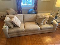 Front and side view of a beige fabric three-seat sofa with cushions in a living room setting.