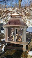 Front view of metal outdoor fireplace showing mesh doors and chimney top with snow accents