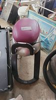 Top view showing purple padded seat and black curved base of the exercise machine surrounded by other items.