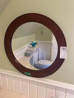 Front view of the circular mirror hanging on a wall, showing its reddish-brown wooden frame.