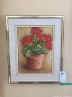 Framed and matted oil painting showing red geranium flowers in a terra cotta pot against a soft background, with no visible signature.