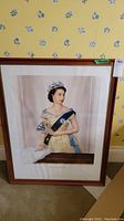 Framed print of Queen Elizabeth II in a yellow gown with blue sash, diamond tiara, and white fur stole. The print is vertically oriented and mounted in a wooden frame with white matting.