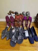 Eight pairs of assorted women's shoes arranged in two rows on floor showing various styles and colors