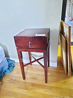 Wooden side table with drawer, showing front and side on hardwood floor against a light wall. Minor scratches on surface visible.