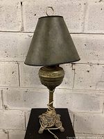 Full view of antique brass table lamp showing overall shape, ornate base, and dark metal tapered shade with finial on top.