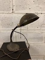 View of the overall antique metal desk lamp showing the dome-shaped lampshade, gooseneck neck, cord and pull chain.