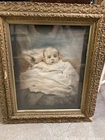 Full view of the antique baby portrait in an ornate gold-tone frame.