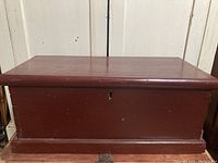 Closed view of the antique wooden tool chest showing reddish-brown finish with keyhole on front.