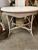 Full view of the white wicker oval top table showing the curved wicker apron and legs.