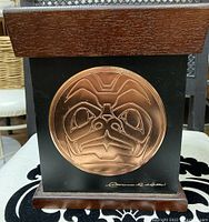 Front view of dark wood box with large circular copper embossed design showing Native West Coast Haida face motif signed by Clarence R Wells.