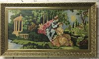 Full view of the large, ornately framed needlepoint artwork showing a couple in historical dress in a garden setting, encased in a decorative gold frame with non-glare glass.