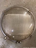 Top-down view of the round glass convex lens within metal frame, showing ribbed glass center and clamps.
