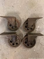 Top-down view of the 4 vintage cast iron caster wheels laid out flat on a concrete floor, showing mounting plates and wheel design.