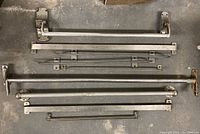 Top-down view of all nine metal door pulls arranged on concrete floor showcasing varying lengths and styles.
