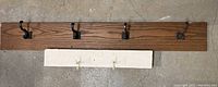 Long wooden board with four black iron hooks mounted on it, laid on floor