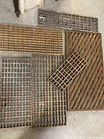 Multiple vintage wooden floor grates laid on concrete floor, showing variety of grid patterns and sizes.