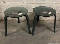 Pair of two-legged round wooden side tables with a hand painted loon design on the tabletop, shown from front angle against wall.
