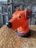 Side profile of the orange plastic dog head sculpture showing facial details and black-shaded ears and nose.