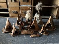Overview of seven miniature First Nations teepees made of stitched leather, some decorated with sticks and fur. Small leather canoe piece is visible.