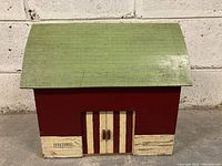 Front view of vintage wooden toy barn with green roof, red walls, beige stone painted lower sections, and closed sliding doors