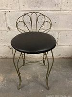 Front view of vintage metal and vinyl vanity stool showing metal decorative backrest and black vinyl cushioned seat.