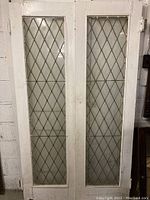 Front view of the pair of tall white wooden doors with diamond pattern leaded glass panels showing overall look and condition.