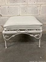 Front view of white vinyl cushioned wrought iron patio stool showing intact cushion on frame with decorative metal loops and twisted metal design on legs.