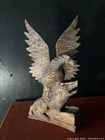 Front view of the hand-carved wooden sculpture showing bird spreading wings perched on animal prey.
