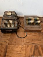 Full view of two connected vintage R.C. Allen machines sitting on wood floor showing keys and metal bodies.