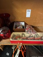 Photo showing vintage Christmas train ornament set in box, small assorted Christmas ornaments, and a plastic bag of additional ornaments on wooden shelf with other items.
