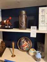 Two shelves of collectibles including a red horse figurine, a dark ceramic abstract face vase, a framed religious art print, various ceramic vases, and a clear glass vase.