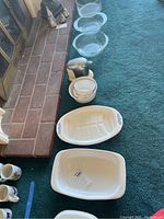 Photo of white Corningware and Pyrex cookware arranged on carpet including casserole dishes, mixing bowls, and smaller bowls.
