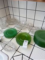 Crystal and green uranium glass plates and bowls arranged on tiled countertop. Displays clear cut crystal glass pieces and stacks of green colored plates.