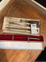 Set of three carving utensils with wooden handles including a fork, knife, and skewer in original box, viewed from above.
