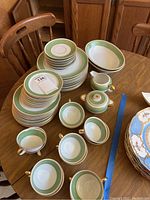 Wide view of full set including stacked plates, bowls, cups, creamer, sugar bowl, and gravy boat on wooden table.