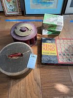 Overall lot showing two wooden containers, a boxed Reno-Keno game, and a poker chip dispenser and holder on wood floor with framed artwork in background.