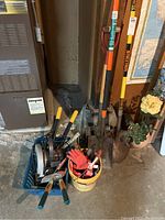Photo of garden tools including shovels, shears, gloves, bucket with small tools, and blue basket with hand and power tools