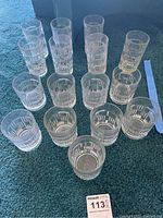 View of all 16 glass tumblers arranged on carpet, showing various heights and sizes with etched geometric pattern.