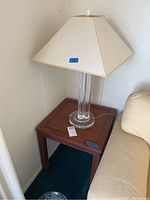 Side corner view showing the wood end table with clear glass column lamp and cream fabric shade beside a beige couch.