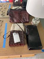 Three purses and one metal container displayed on wooden surface with small jewelry items visible in background.