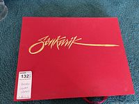 Red slipcase with gold foil Senkarik logo on top and auction label on corner.