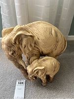 Elephant statue with baby elephant figurine on carpeted floor near window curtains, showing front and side views.