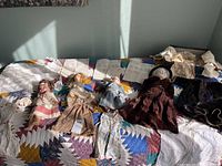 Four vintage dolls displayed on a quilted bedspread with appraisal papers and additional doll clothes.