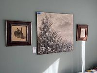 Three pieces of wall art displayed on green wall, including large floral canvas and two smaller framed animal/figure drawings.