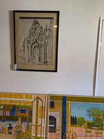 Three framed wall art pieces displayed on a white wall. One is an architectural sketch and another is a scenic colorful print.