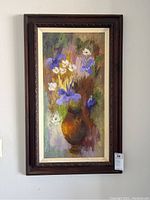Image of framed floral painting showing purple and white flowers in a brown vase, with dark brown carved frame and cream inner border