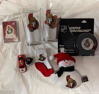Photo of Ottawa Senators collectible items including cards in a tin, two glasses, trivia puck game, toy car, helmet, socks, and snowman plush.