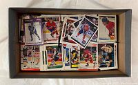 Top-down view of a box filled with over 1,300 assorted hockey trading cards showing various players and teams.