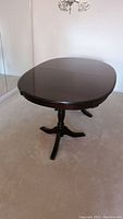 Oval dark wood dining table pictured from an angle, showing glossy surface and double pedestal leg
