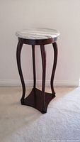 Front-side view of plant stand showing round marble top and wooden curved legs
